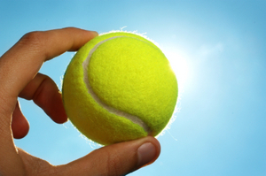 Hand holding tennis ball up to the sky